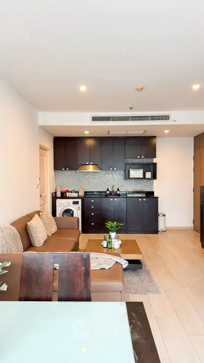 Modern living room with open kitchen and washing machine, featuring sleek furniture and stylish decor.