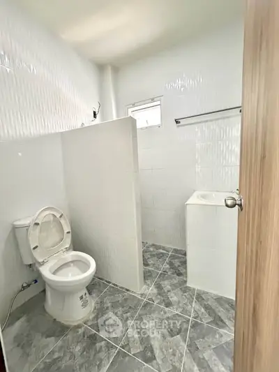 Modern bathroom with tiled walls and floor, featuring a toilet and a small window for natural light.