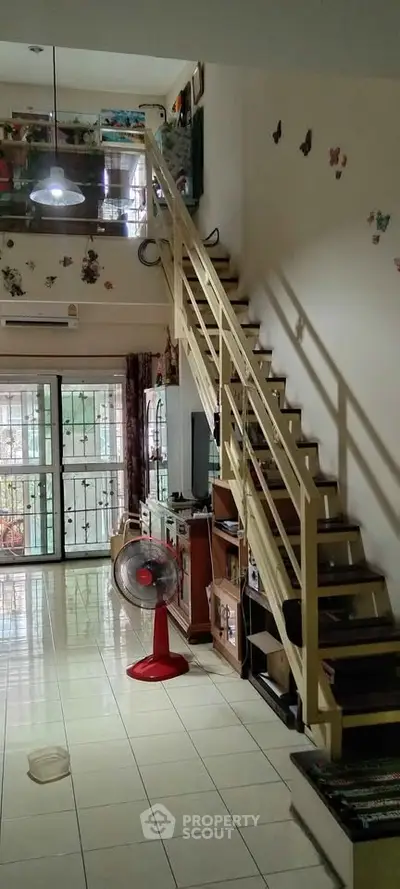 Spacious living room with staircase and balcony access, featuring tiled flooring and natural light.