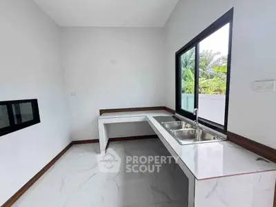 Modern minimalist kitchen with dual sink and large window overlooking greenery.