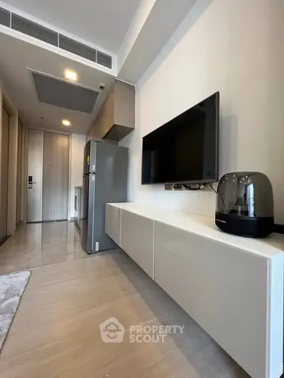 Modern apartment interior with sleek TV setup and stainless steel fridge.