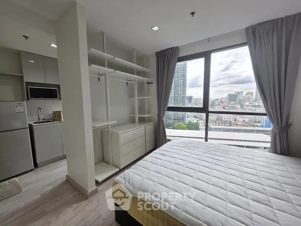 Modern bedroom with city view, open closet, and adjacent kitchen area in a high-rise apartment.