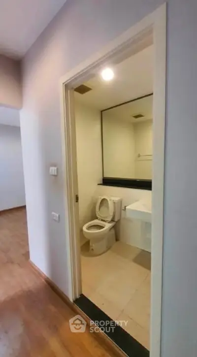 Modern bathroom with sleek design and wooden flooring in adjacent area.