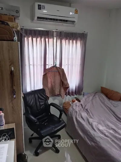 Cozy bedroom with air conditioning and natural light through curtains, featuring a comfortable chair and tidy bed.