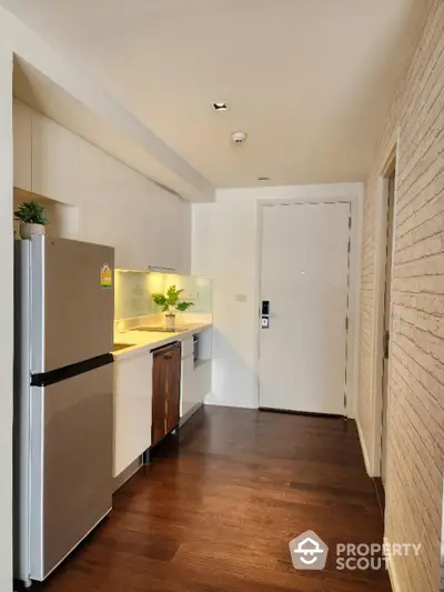 Modern kitchen with stainless steel appliances, sleek cabinetry, and warm wooden flooring complemented by chic brickwork walls.