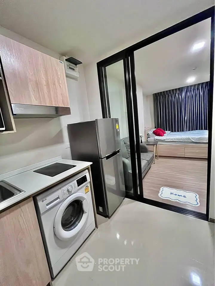 Modern apartment with open kitchen and cozy living area featuring washing machine and fridge.