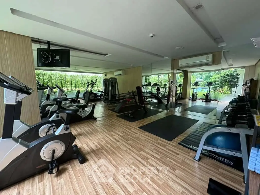 Spacious gym with modern equipment and large windows overlooking greenery, perfect for fitness enthusiasts.