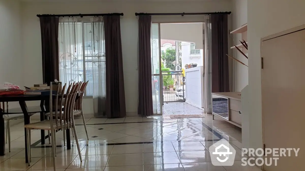 Spacious living room with glossy tiled flooring, large windows draped with elegant curtains, and a dining area leading to a bright patio.