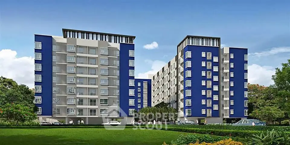 Modern apartment complex with blue and white facade, lush green surroundings, and ample parking space.