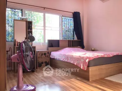 Cozy bedroom with wooden flooring and large window, featuring a stylish bed and fan.