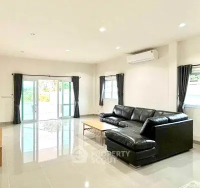 Spacious modern living room with sleek black leather sofa and large windows for natural light.