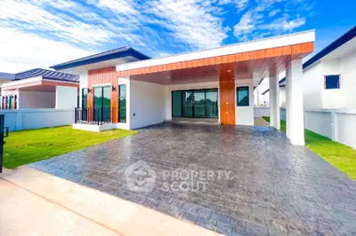 Modern single-story home with spacious driveway, elegant wooden accents, and lush green lawn under a clear blue sky.