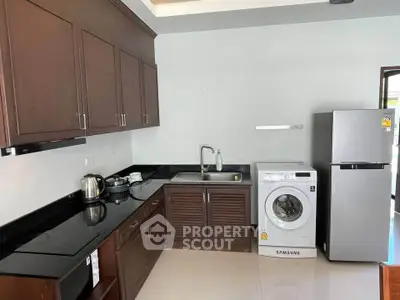 Modern kitchen with wooden cabinets, washing machine, and stainless steel fridge