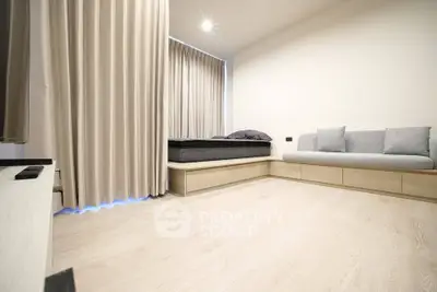 Modern minimalist bedroom with light wood flooring and cozy seating area.