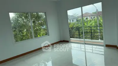 Spacious empty room with large windows and balcony access, offering lush garden views.