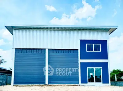 Modern industrial warehouse with blue and white facade, featuring large roller doors and windows.