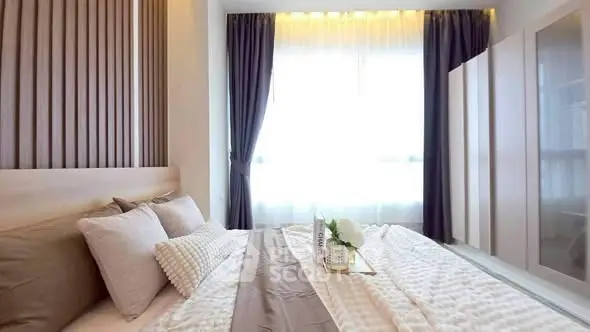 Elegant bedroom with cozy bedding and ample natural light through large window.