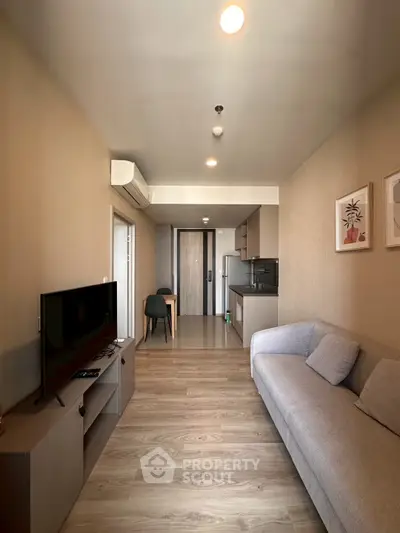 Modern living room with cozy sofa and TV, open layout leading to a stylish kitchen.