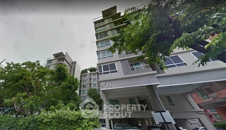 Modern residential building with lush greenery and spacious parking area.
