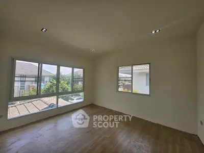Spacious empty room with large windows and wooden flooring, offering ample natural light and serene views.