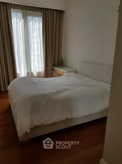 Cozy bedroom with elegant wooden flooring and natural light through large window.