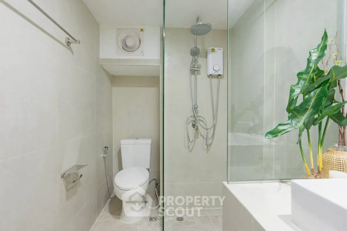 Modern bathroom with sleek design, featuring a shower, toilet, and stylish plant decor.