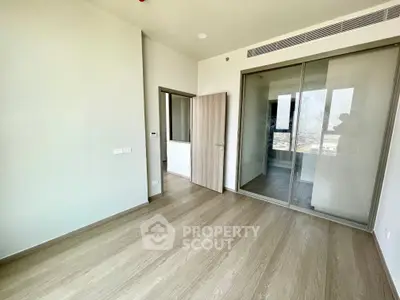 Spacious modern bedroom with wooden flooring and mirrored closet doors in a high-rise apartment.
