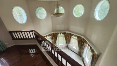 Elegant two-story living room with circular windows and chandelier, featuring hardwood floors and luxurious drapery.