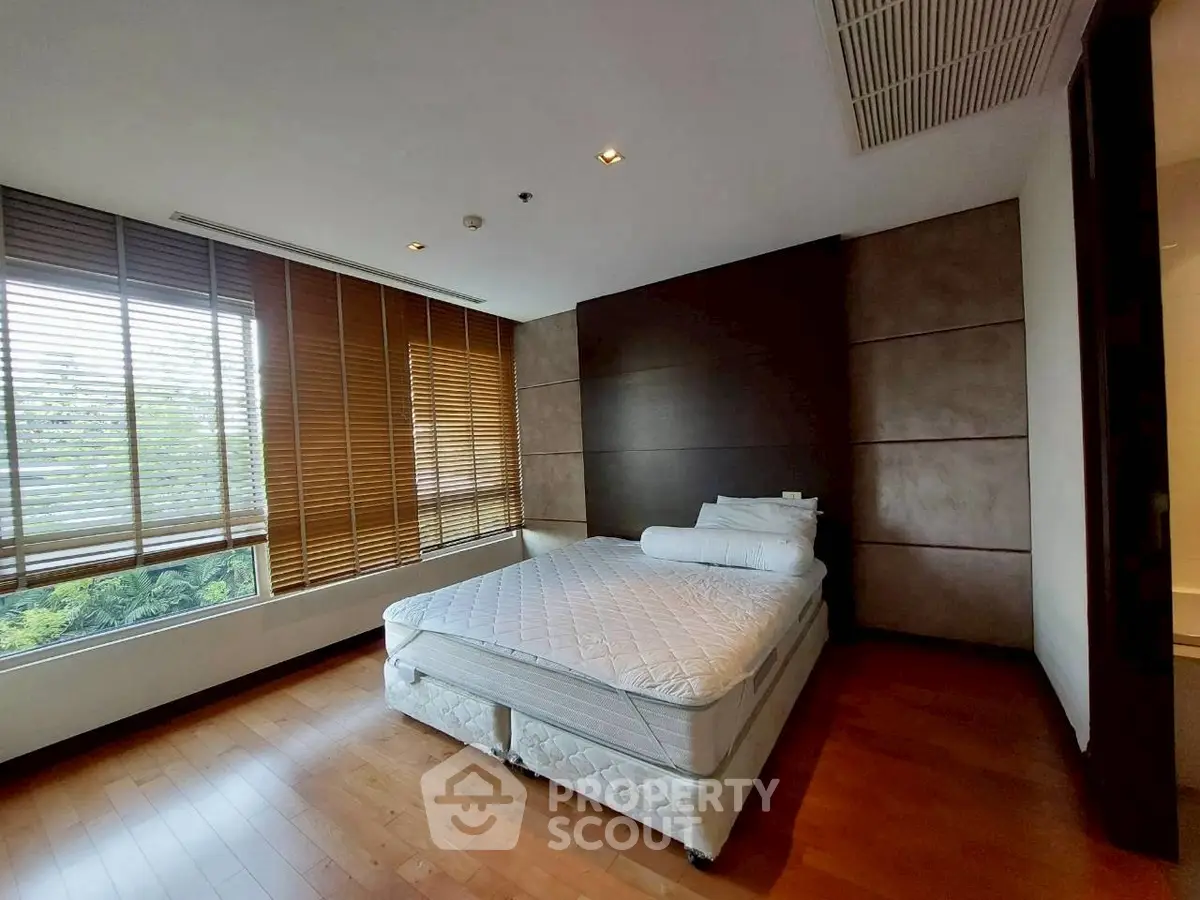 Spacious bedroom with large windows and wooden flooring in modern apartment