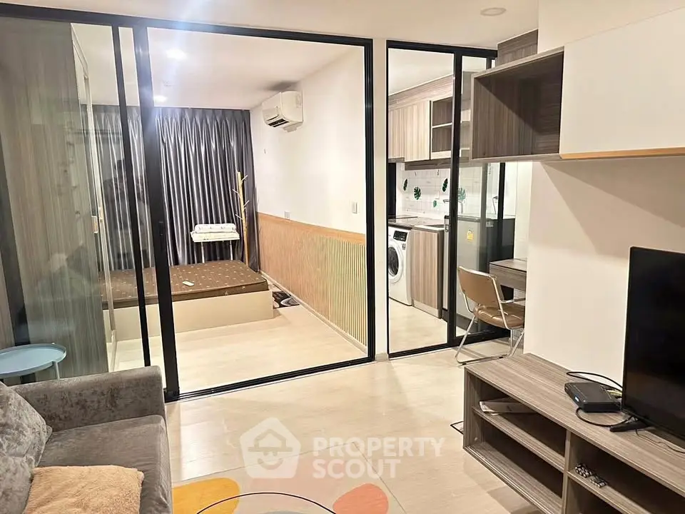 Modern apartment interior with glass partition, cozy living area, and compact kitchen featuring washing machine.