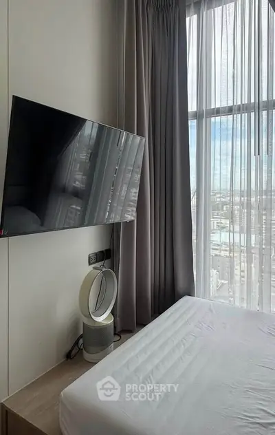 Modern bedroom with large window and city view, featuring a wall-mounted TV and sleek air purifier.
