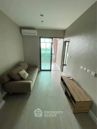 Modern living room with cozy sofa and wooden TV stand, leading to a bright balcony view.