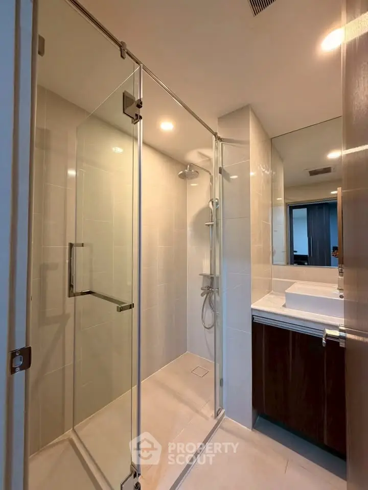 Modern bathroom with glass shower enclosure and sleek vanity in contemporary apartment.