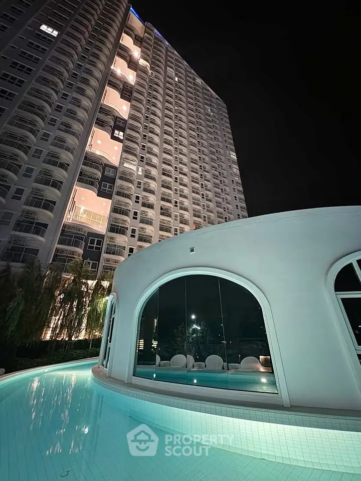 Stunning night view of modern high-rise building with illuminated pool area, perfect for luxury living.
