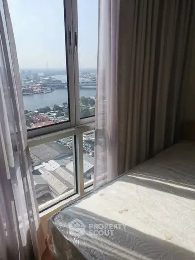 High-rise bedroom with stunning river view through large window, offering natural light and serene ambiance.