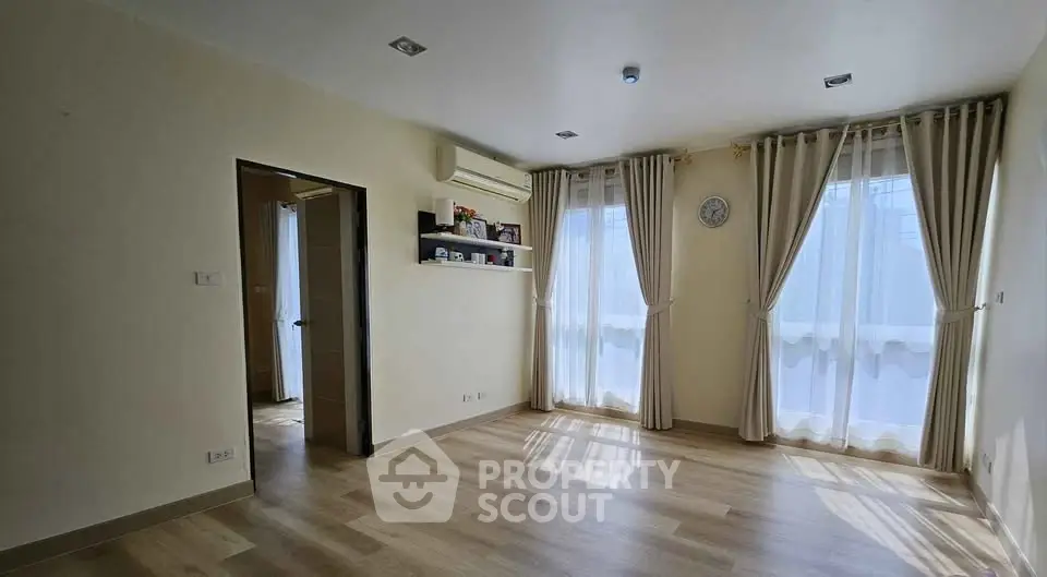 Spacious empty room with wooden flooring and large windows with curtains