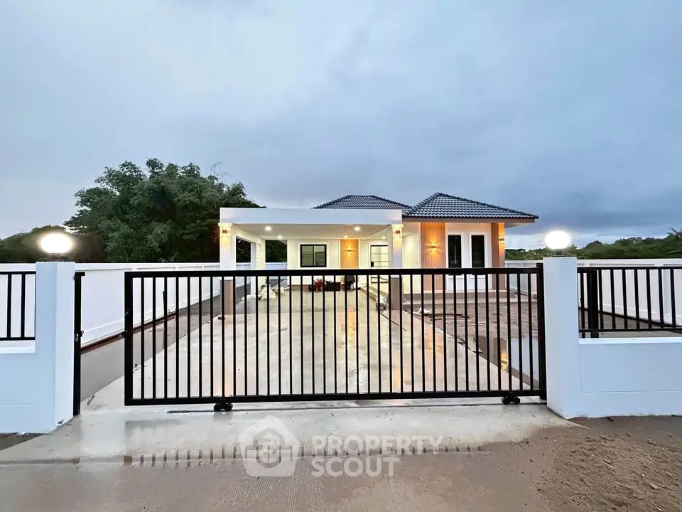 Modern single-story house with gated entrance and spacious driveway at dusk.