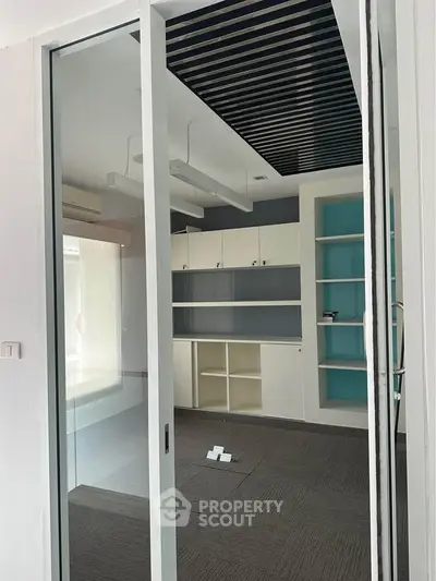 Modern office space with glass sliding door and built-in shelves, ideal for a productive work environment.