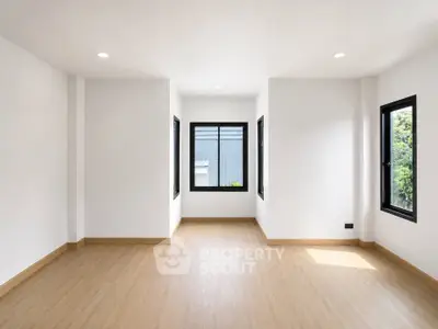 Spacious empty room with large windows and wooden flooring, perfect for customization.