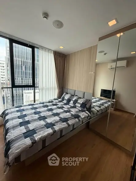 Modern bedroom with large mirrored wardrobe and city view, featuring stylish bedding and wooden flooring.