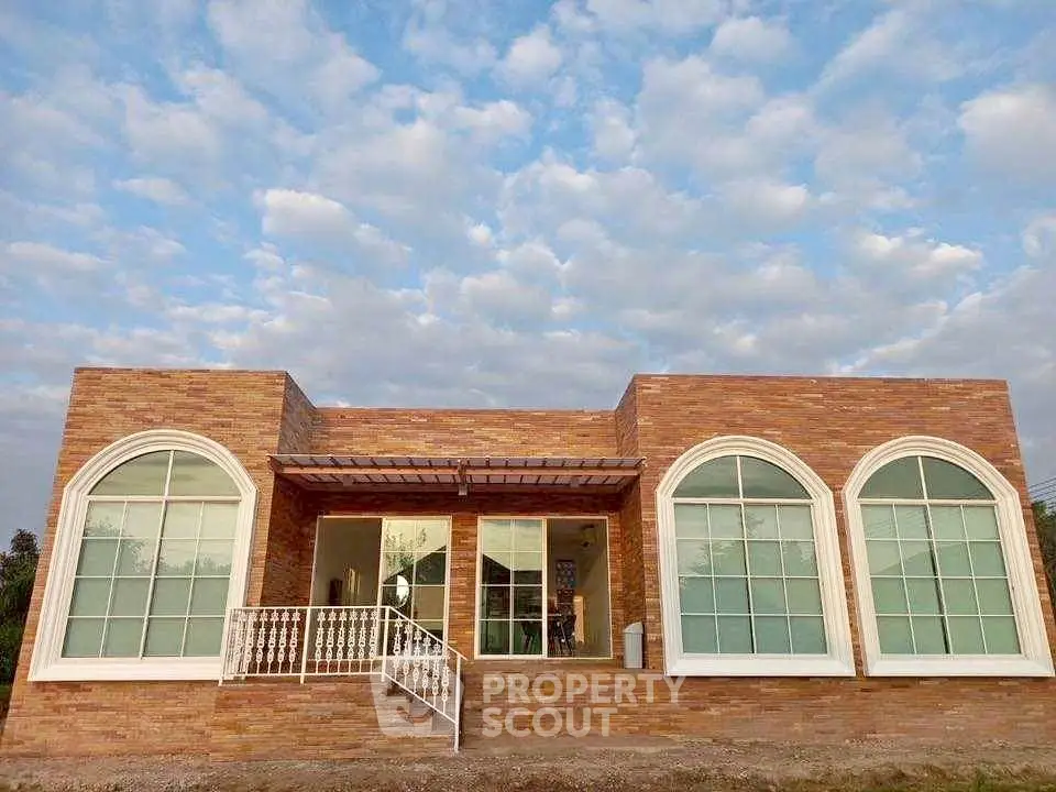 Charming single-story brick house with large arched windows and serene sky backdrop.