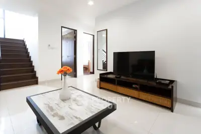 Modern living room with sleek TV stand, stylish coffee table, and elegant staircase in a bright, open space.