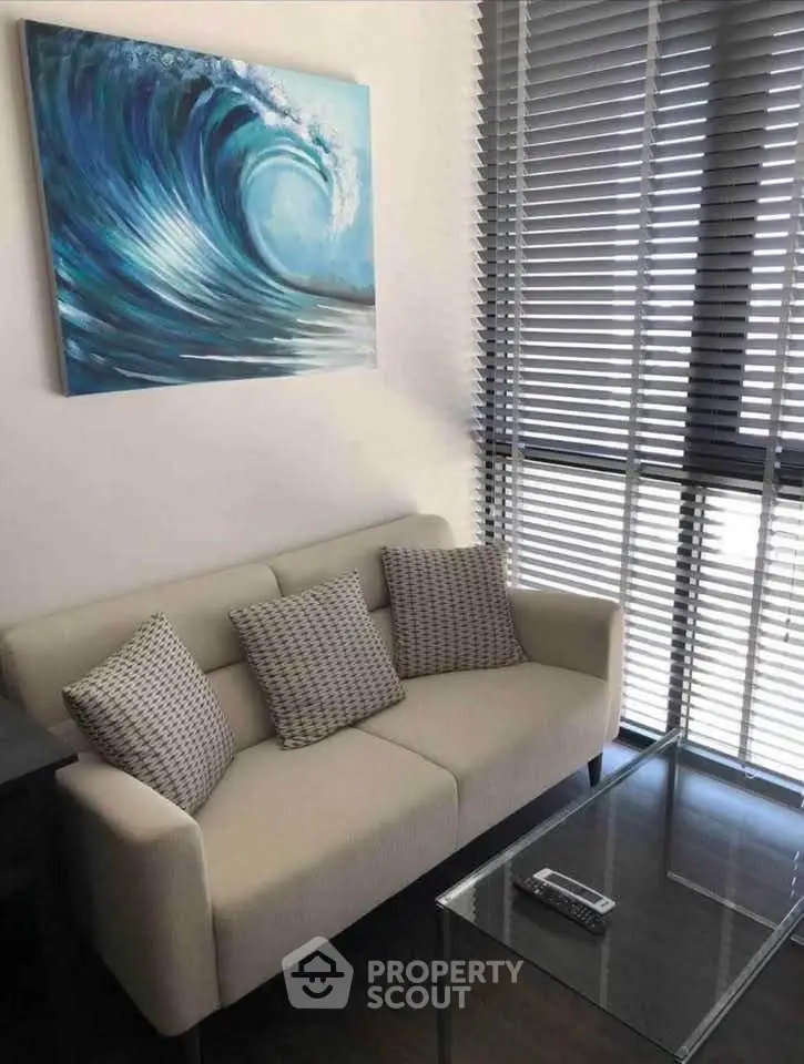 Modern living room with stylish sofa, glass coffee table, and wave artwork, perfect for relaxation.
