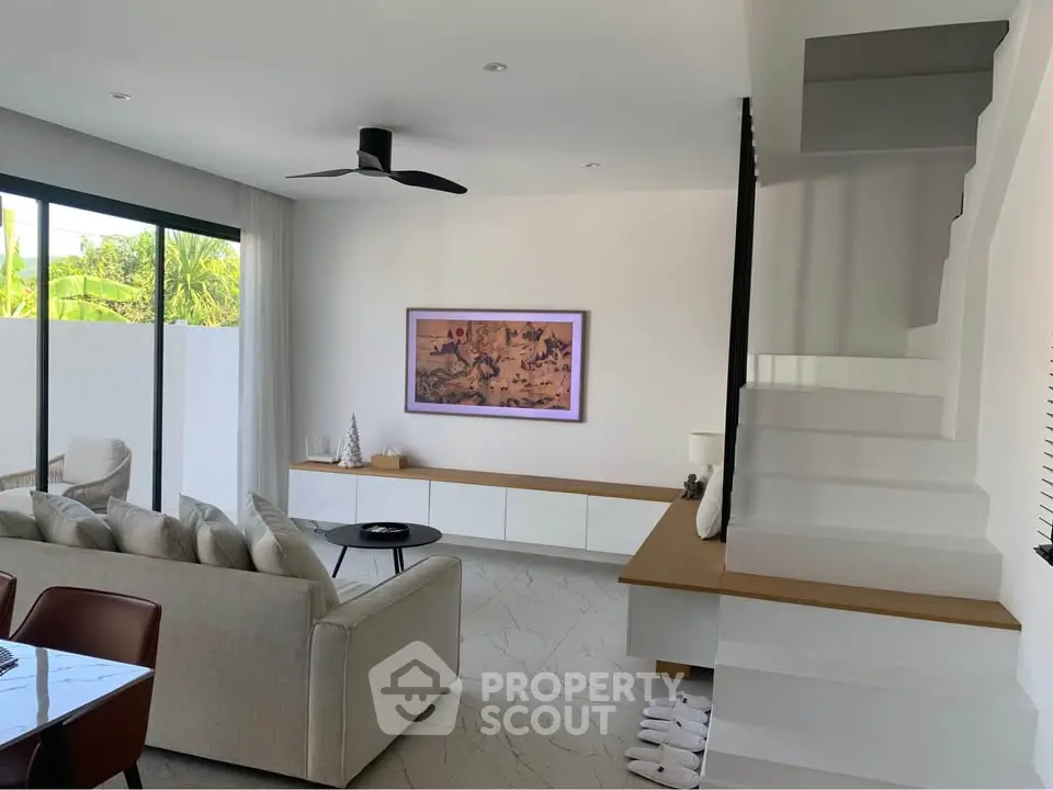 Modern living room with sleek staircase and stylish decor, featuring large windows and contemporary furniture.