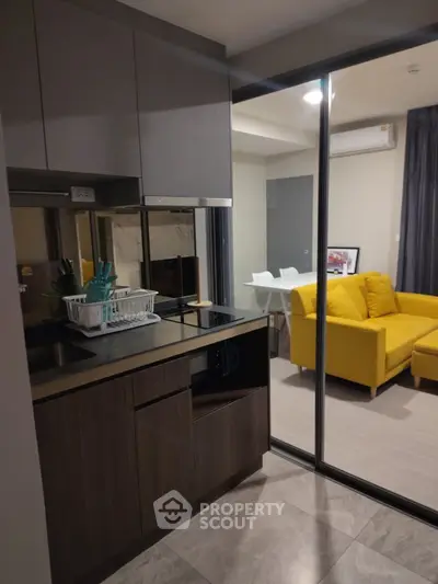 Modern kitchen with sleek cabinets and open layout adjacent to cozy living room with yellow sofa.
