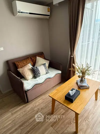 Cozy living room with air conditioning and natural light, featuring a comfortable sofa and wooden coffee table.