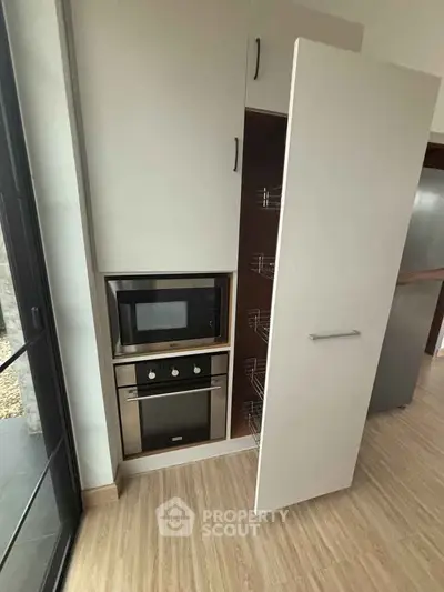 Modern kitchen with built-in oven and microwave, sleek cabinetry, and wooden flooring.