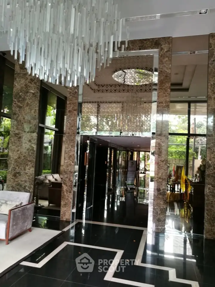 Luxurious building entrance with elegant marble and glass design, featuring a stunning chandelier and modern decor.