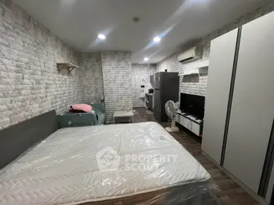 Modern studio apartment with stylish brick walls and compact layout, featuring a bed, sofa, and kitchen area.