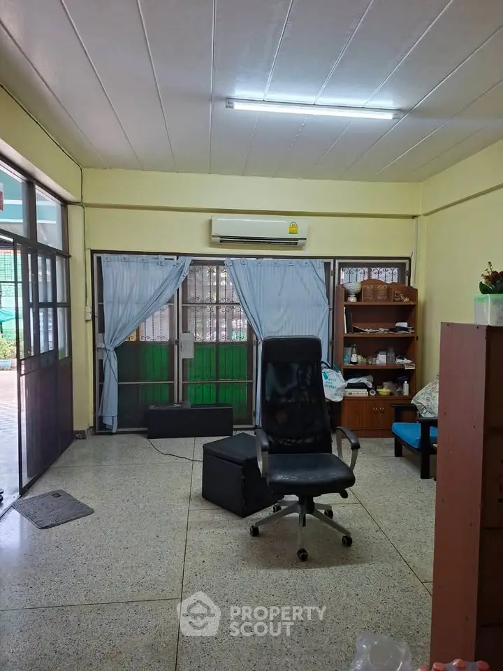 Spacious living room with natural light, featuring a comfortable office chair and large windows.